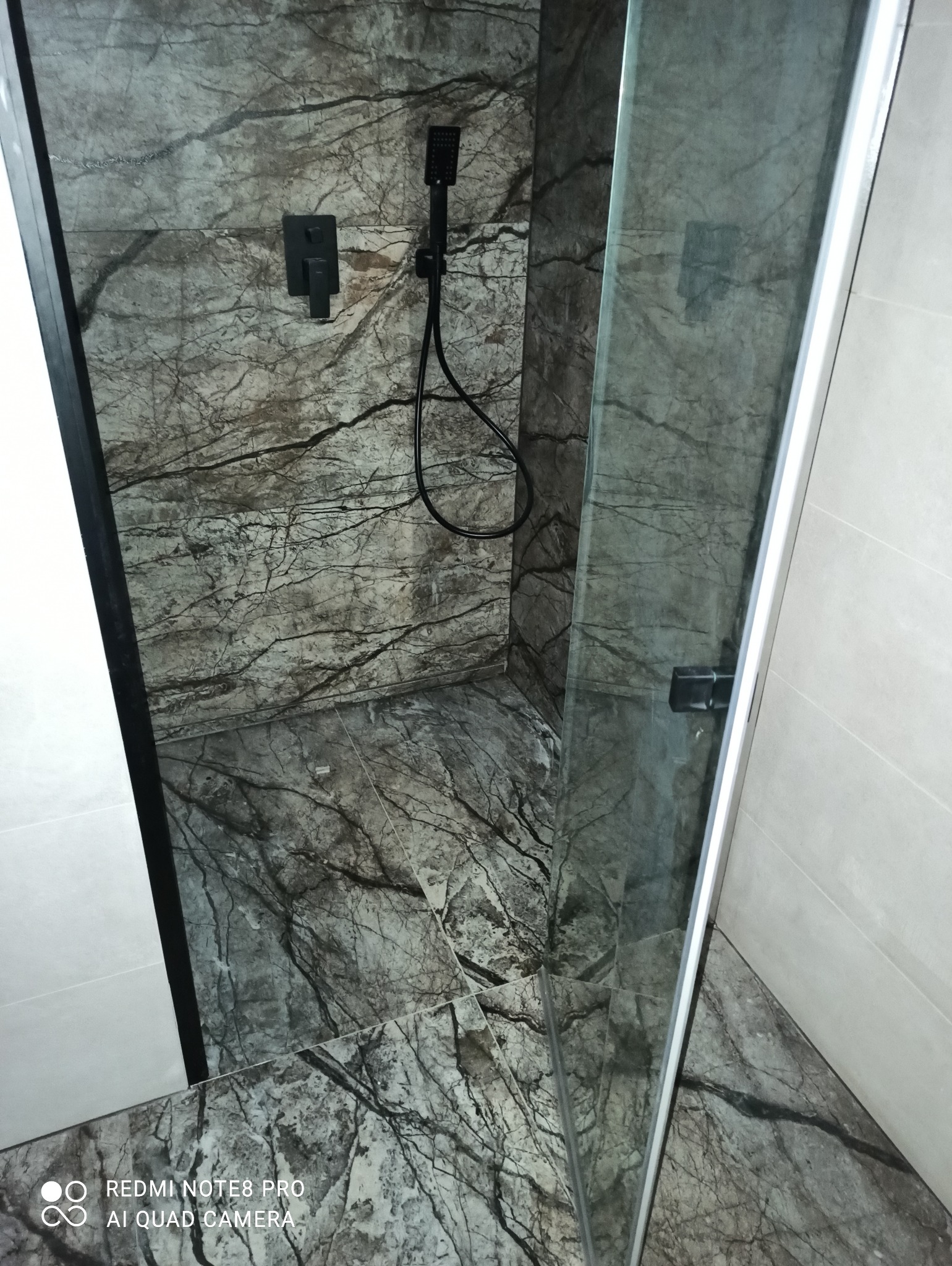 Kabina prysznicowa walk-in z czarną armaturą i płytkami imitującymi marmur w Dzierżążnie. Widoczny szklany panel i minimalistyczny design.