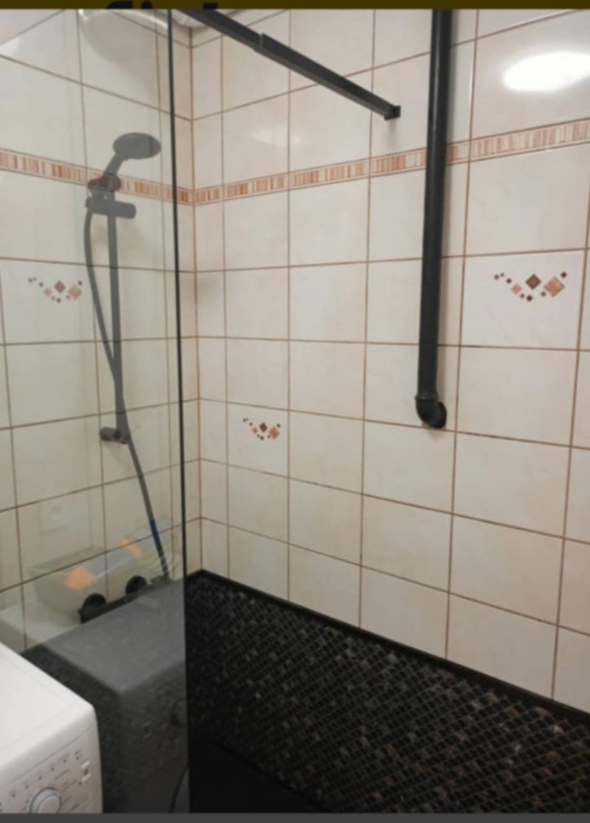 Umyta kabina prysznicowa z czarną armaturą i czarną mozaiką na podłodze, widoczna pralka z boku.