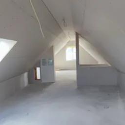 Poddasze w trakcie wykańczania, ściany i sufit pokryte płytami gipsowo-kartonowymi, widoczne okno dachowe i instalacje elektryczne.