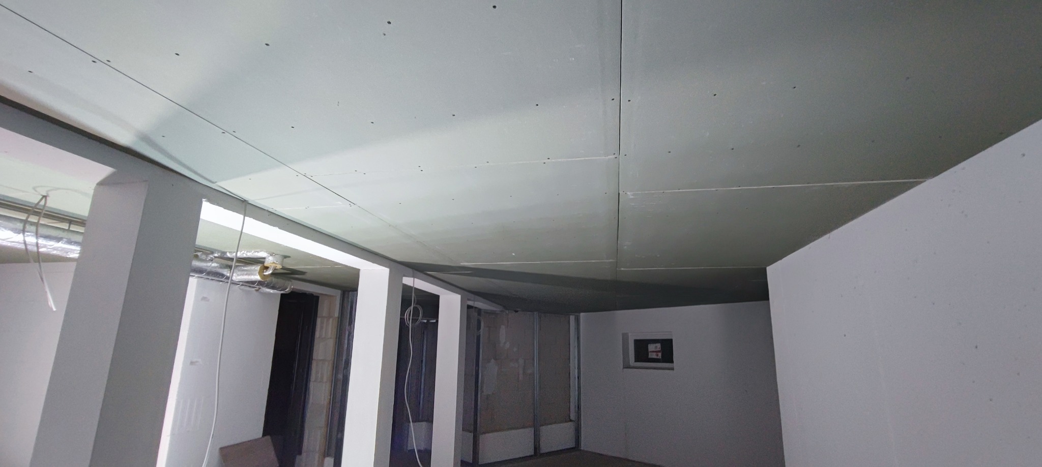 Sufit z płyt kartonowo-gipsowych z widocznymi łączeniami i śrubami, w trakcie montażu, widoczne metalowe profile i instalacje wentylacyjne w tle.