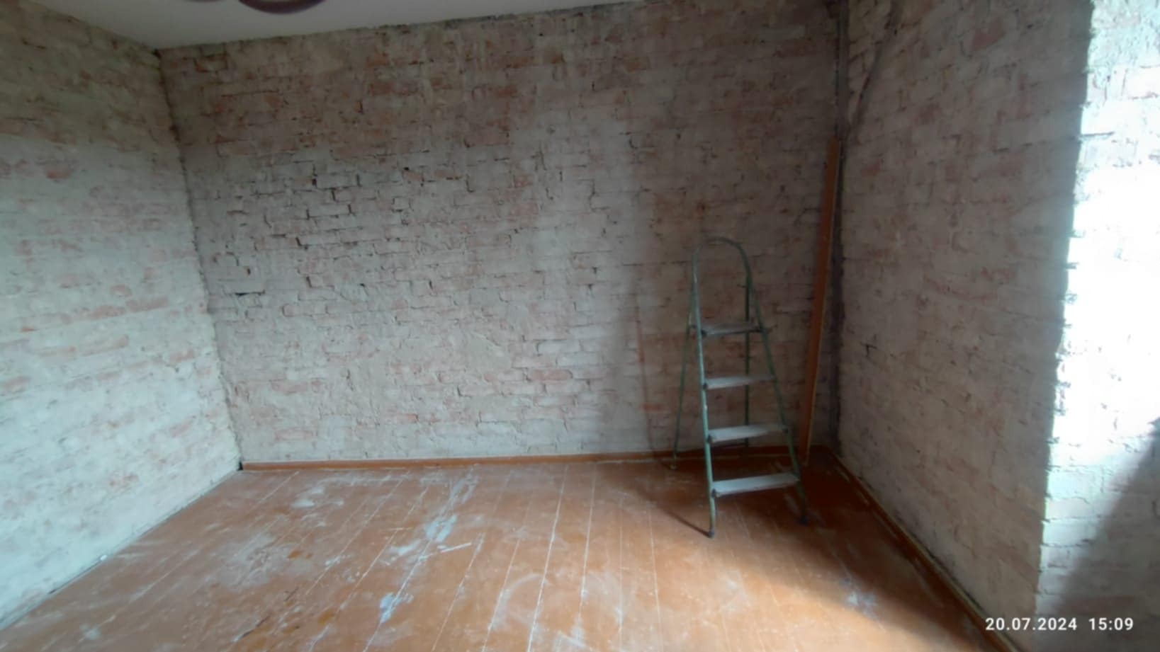 Pokój przed remontem: surowe, częściowo otynkowane ceglane ściany, drewniana podłoga, drabina przystawna w rogu.