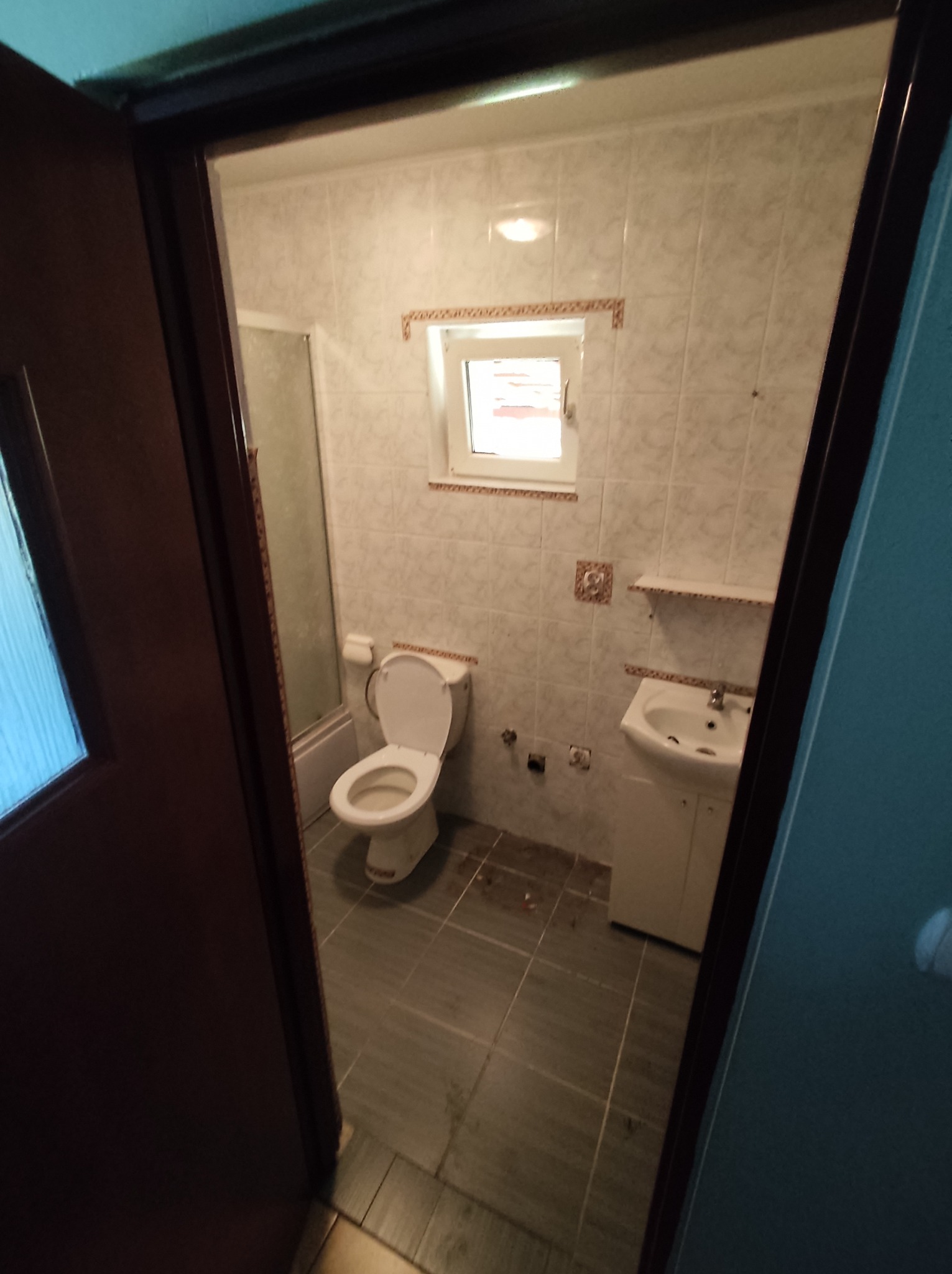 Widok na odnowioną łazienkę z kabiną prysznicową, umywalką z szafką i toaletą, sfotografowaną zza uchylonych drzwi z widocznym fragmentem futryny.