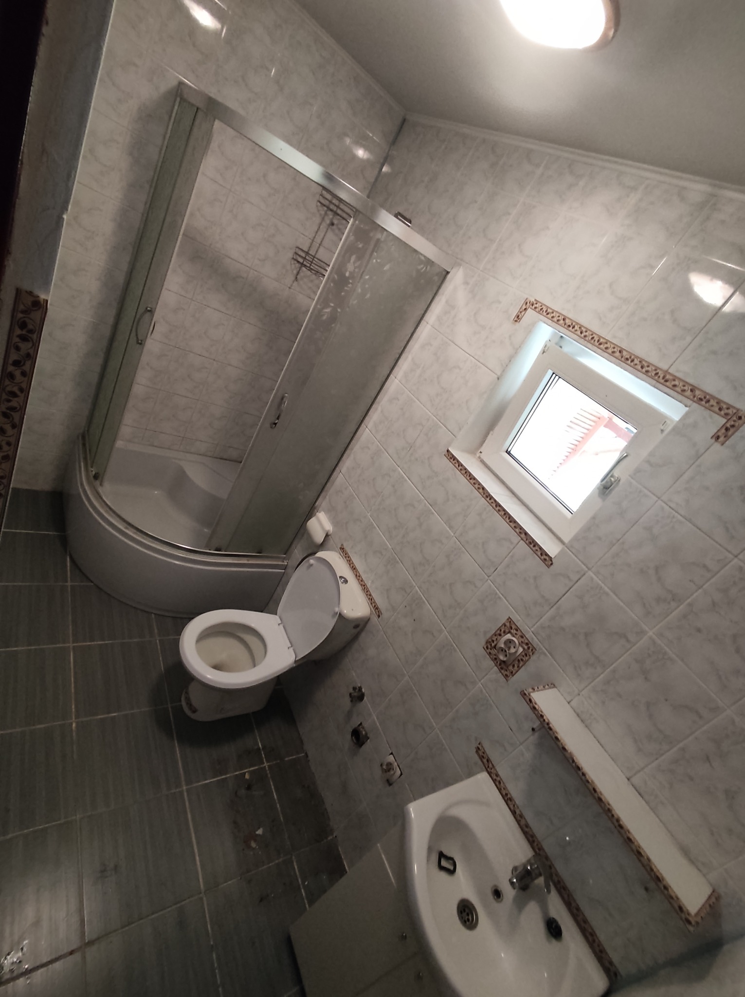 Ukończona łazienka z kabiną prysznicową, toaletą i umywalką, wykończona płytkami w odcieniach szarości i bieli, widok z góry, z widocznym oknem w tle.