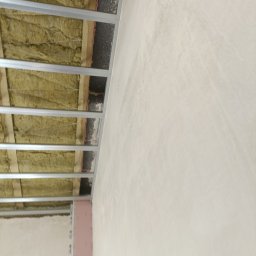 POZIOM JEST V. MIK & A. SPANCHAK S.C. - Szkielet sufitu podwieszanego z izolacją z wełny mineralnej, widoczna ściana z surową powierzchnią przed wykończeniem.