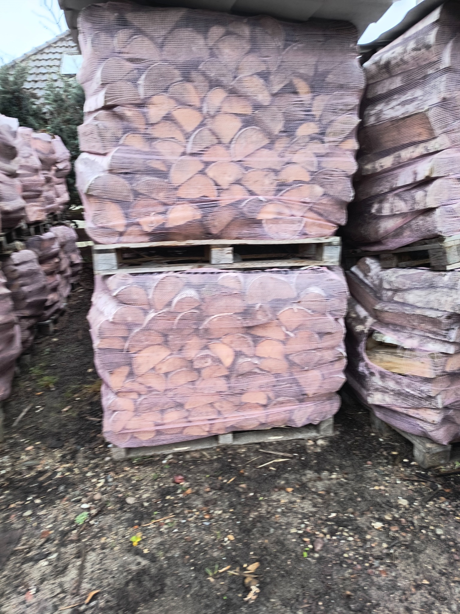 Pakiety drewna kominkowego ułożone na paletach, zabezpieczone siatką, składowane w Papierni, widok z bliska.