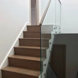 Schody drewniane z przezroczystą balustradą szklaną mocowaną na metalowych uchwytach, widok z dołu, jasne wnętrze.