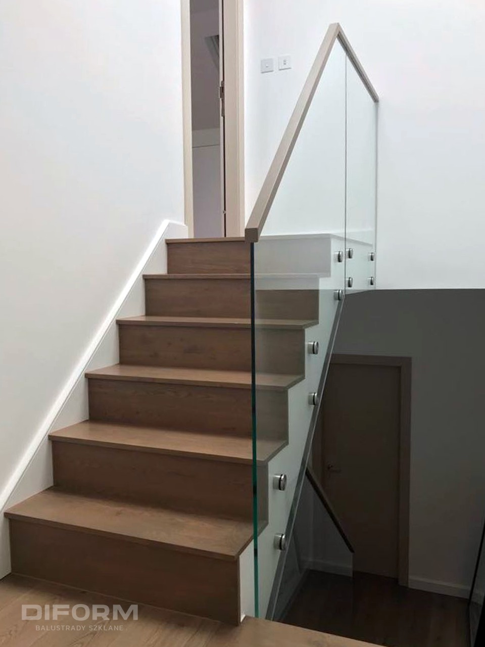 Schody drewniane z przezroczystą balustradą szklaną mocowaną na metalowych uchwytach, widok z dołu, jasne wnętrze.