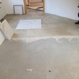 DudziakFach - Przygotowanie podłoża pod płytki w pomieszczeniu, widoczne płyty z wzorem marmuru, wylewka wyrównująca i fragment podłogi z pozostałościami po kleju.