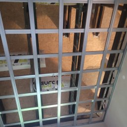 DudziakFach - Szkielet sufitu podwieszanego z profili metalowych w skośnym poddaszu, widoczne płyty OSB i izolacja. Konstrukcja przygotowana do montażu płyt karton-gips.