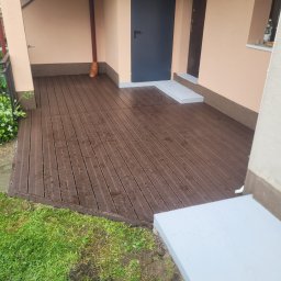 DudziakFach - Wykończony taras z desek kompozytowych w Kamionnej. Nowoczesny design, brązowe deski, jasne obramowanie. Estetyczne połączenie z zielenią ogrodu.