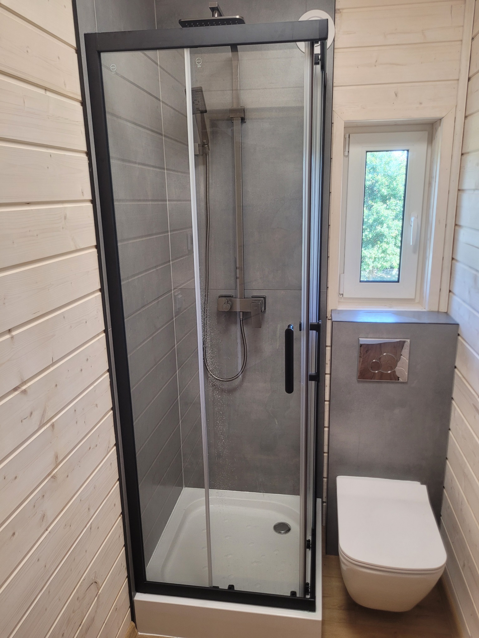 Nowoczesna kabina prysznicowa z czarnymi profilami i toaleta w wykończonej łazience w Kamionnej. Ściany wyłożone płytkami imitującymi drewno.