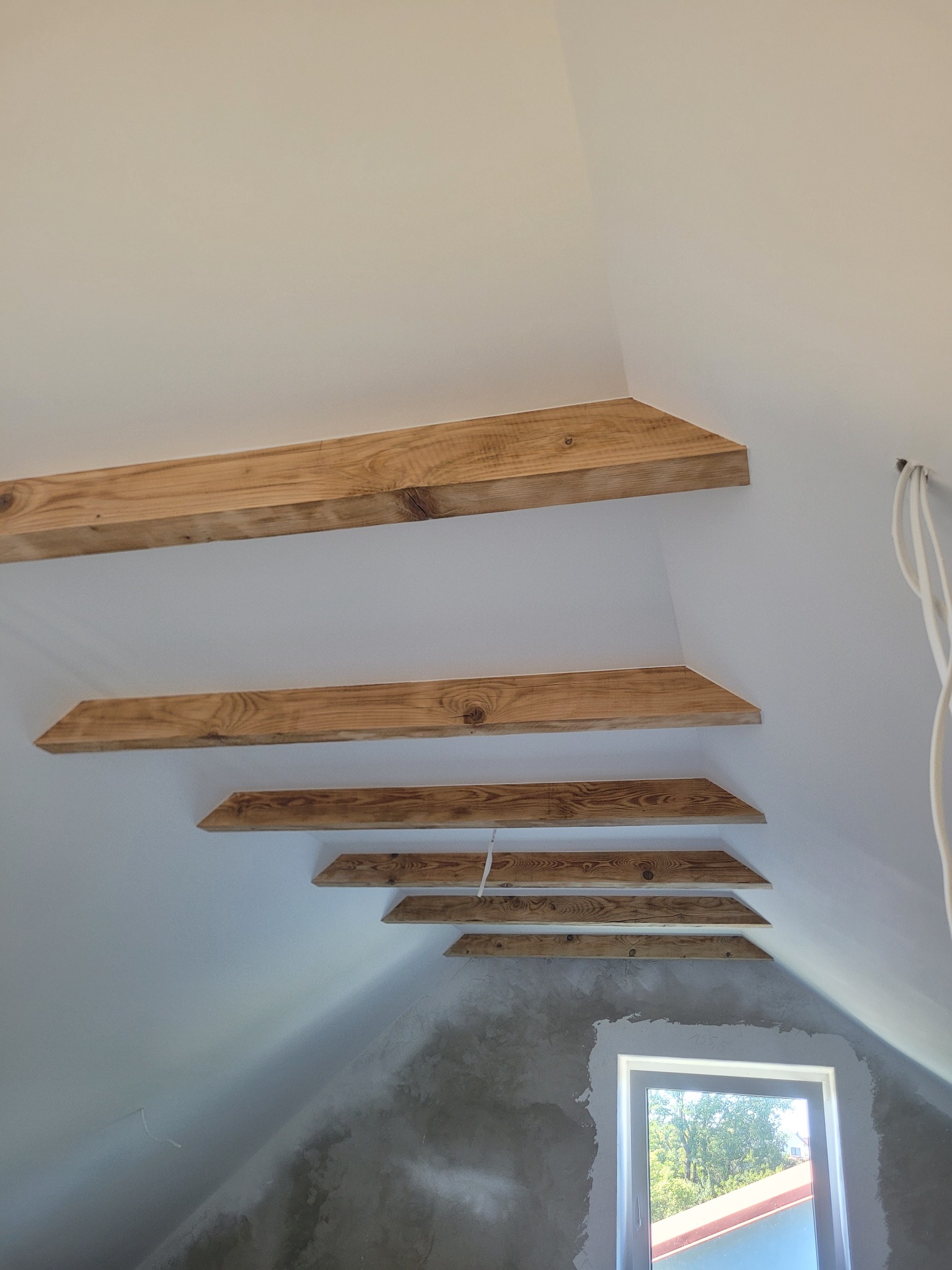 Wykończone drewniane belki na poddaszu, widok z dołu. Szpachlowane ściany i okno w tle. Element dekoracyjny w jasnym wnętrzu.