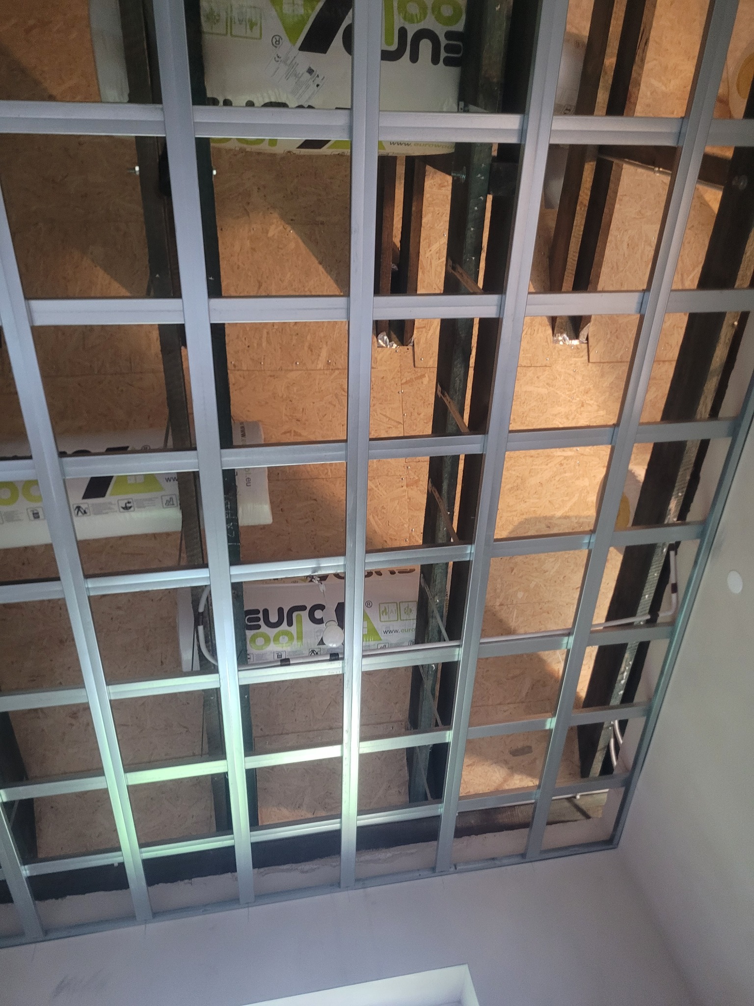 Szkielet sufitu podwieszanego z profili metalowych w skośnym poddaszu, widoczne płyty OSB i izolacja. Konstrukcja przygotowana do montażu płyt karton-gips.