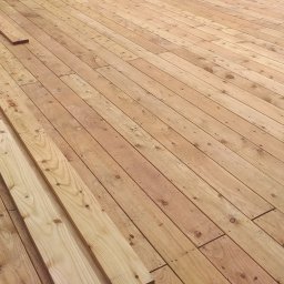 VIKING ŁUKASZ ZIMKOWSKI - Deski tarasowe z widocznym etapem montażu, narzędzia pracy w tle, jasne drewno.