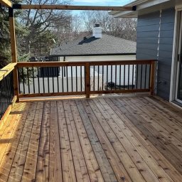 VIKING ŁUKASZ ZIMKOWSKI - Nowy taras z desek z drewna, czarne metalowe balustrady, widok na dom z szarą elewacją i białą balustradą w tle.