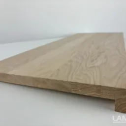 Surowy stopień schodowy z jasnego drewna dębowego z widoczną strukturą słojów, profilowany na krawędzi, leżący na białym tle, z logo producenta w prawym dolnym rogu.