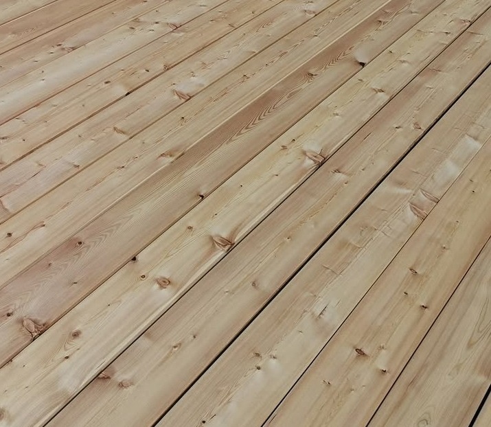 Jasne, drewniane deski tarasowe ułożone ukośnie, widoczne sęki i naturalny rysunek drewna.