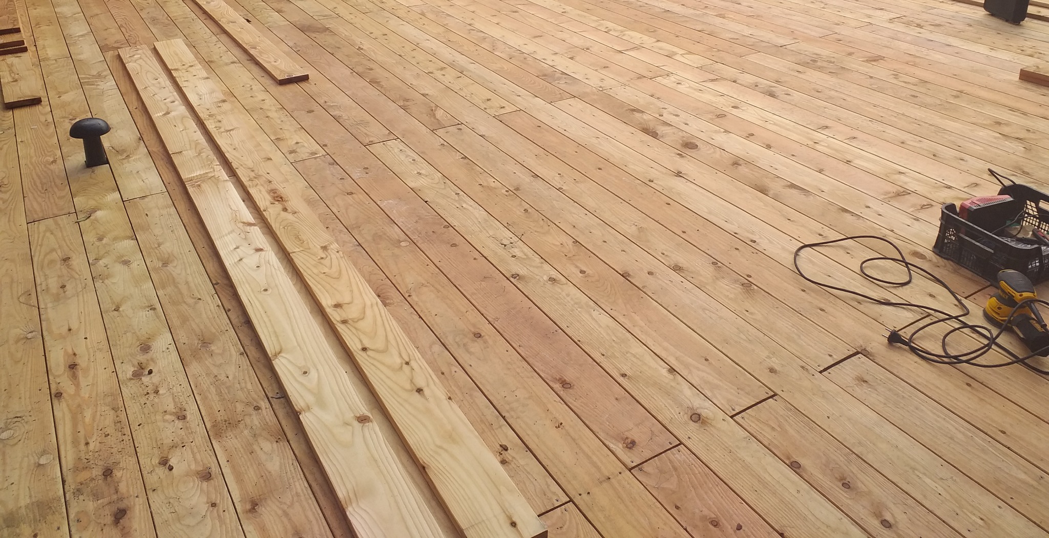 Deski tarasowe z widocznym etapem montażu, narzędzia pracy w tle, jasne drewno.