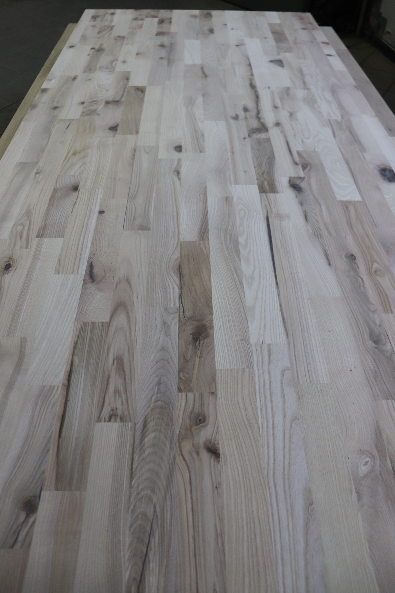 Blat z klejonego drewna jesionowego, widoczne sęki i naturalny układ słojów, ułożony z prostokątnych elementów.