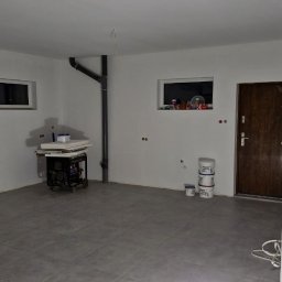 Artur Szypuła - Wnętrze pokoju w trakcie odświeżania: widoczne świeżo pomalowane ściany na biało, szare płytki na podłodze, oraz przygotowane farby i agregat malarski.