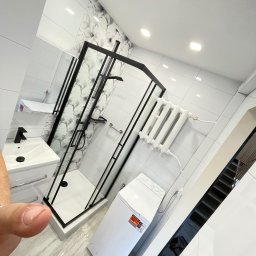 Michal Halas - Nowoczesna łazienka po remoncie: białe płytki, kabina prysznicowa z czarnymi ramami, umywalka z szafką i pralka. Na ścianie płytki z motywem kwiatowym.