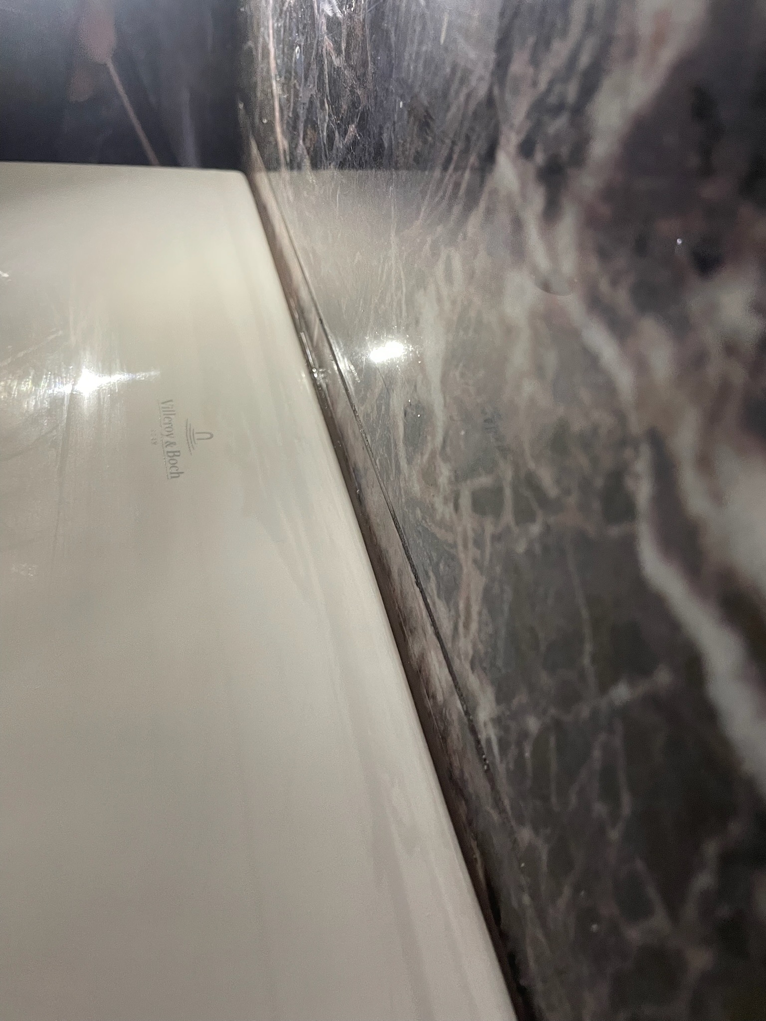 Biała umywalka Villeroy & Boch przylegająca do ściany z ciemnego marmuru w łazience, widok z bliska, oświetlenie górne.