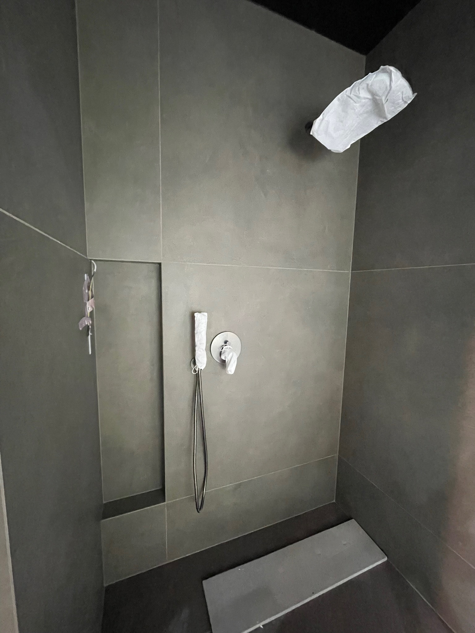 Nowoczesna kabina prysznicowa z szarymi płytkami, deszczownicą i minimalistyczną armaturą. Widoczne zabezpieczenia na armaturze i deszczownicy.