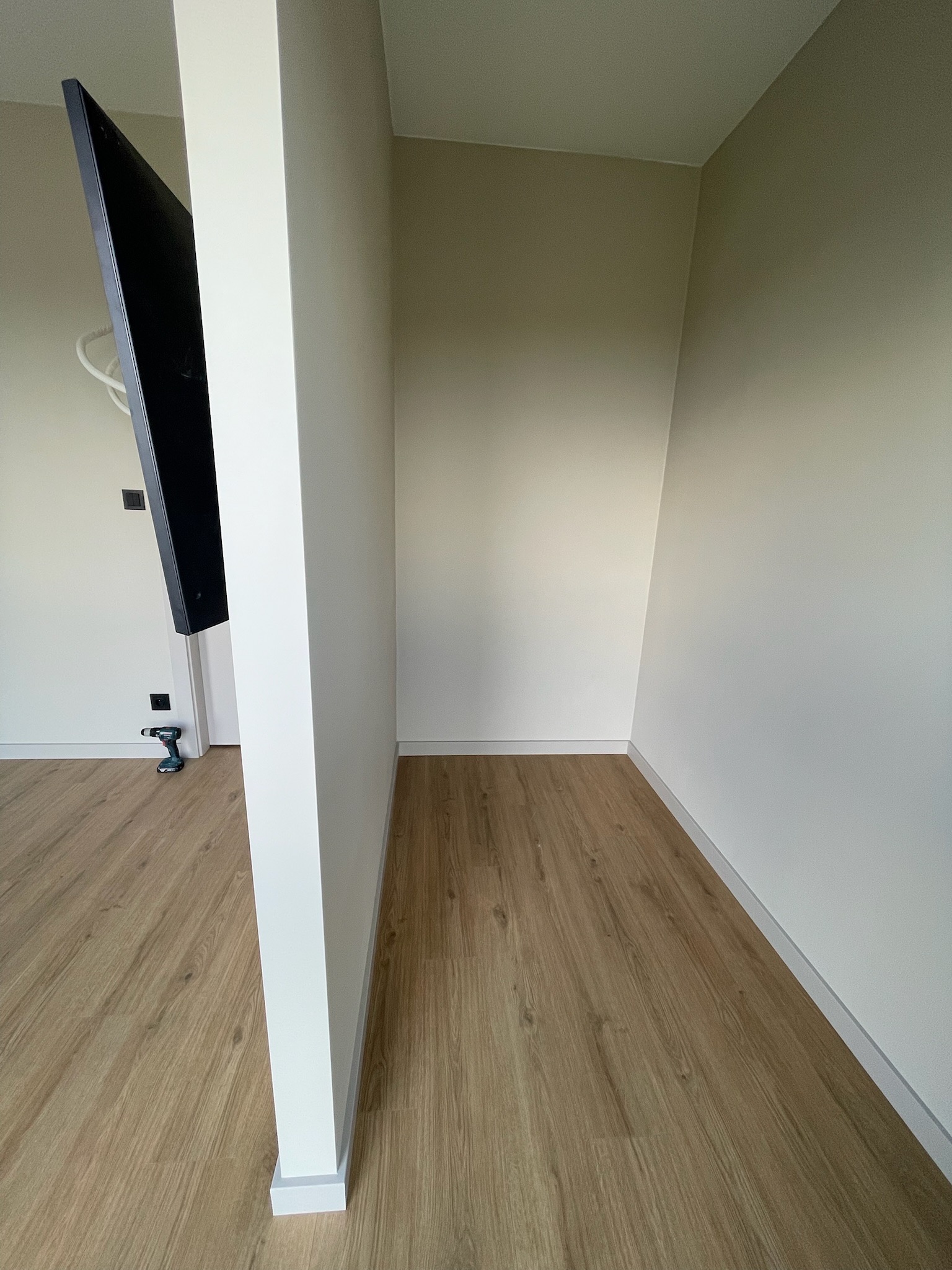Wnętrze po remoncie: drewniana podłoga, świeżo pomalowane ściany w odcieniach bieli i beżu, zamontowany telewizor i wkrętarka na podłodze.