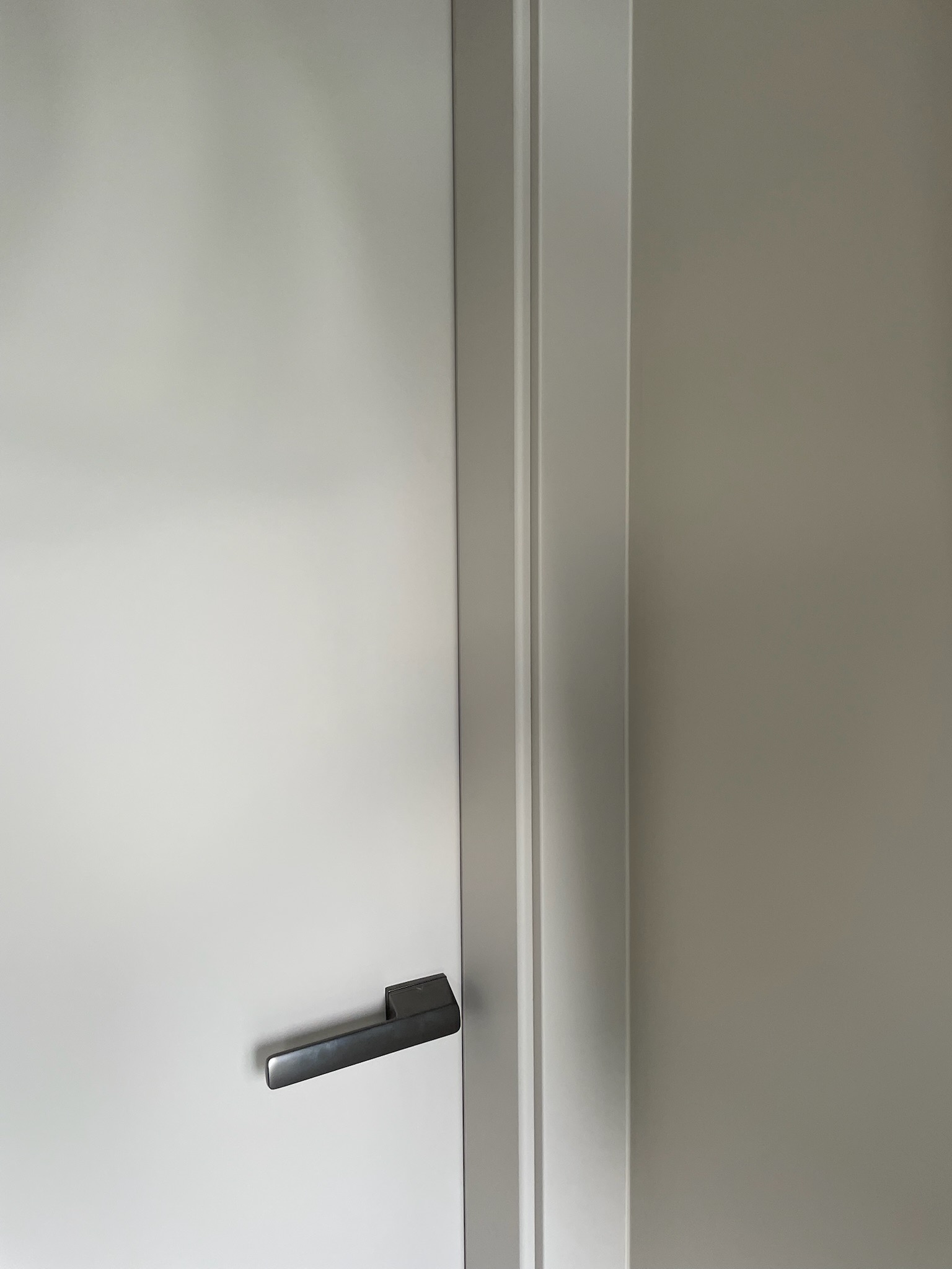 Minimalistyczne, szare drzwi wewnętrzne z metalową klamką, widoczne z bliska. Proste linie i stonowana kolorystyka podkreślają nowoczesny design.