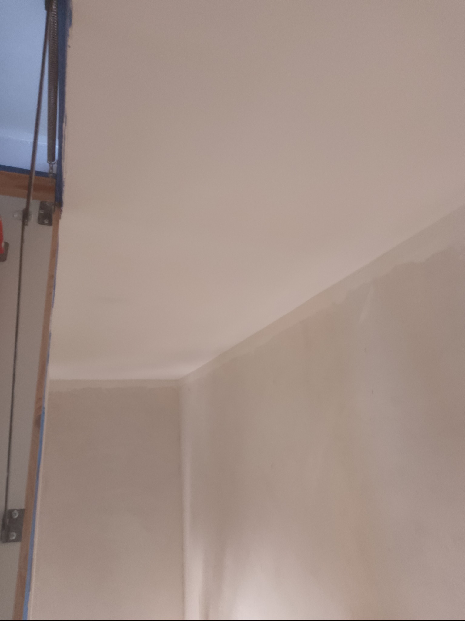 Świeżo położony, gładki tynk na ścianach i suficie w narożniku pomieszczenia, widoczne ślady po taśmie malarskiej przy framudze drzwi.