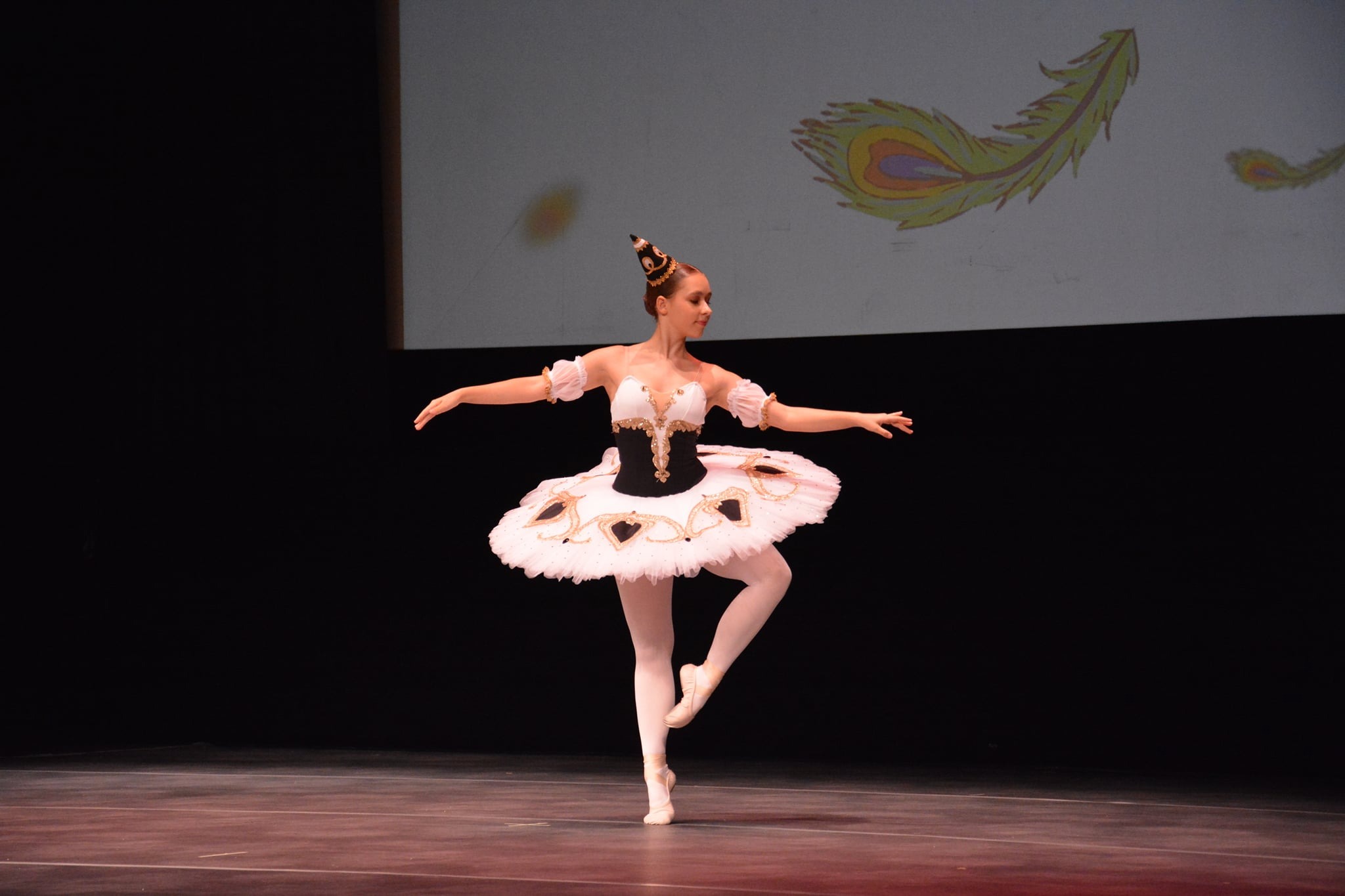 Baletnica w kostiumie na scenie, w tle wyświetlane pióra pawie.