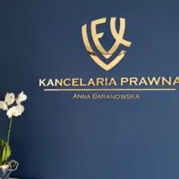 Ściana w kolorze granatowym z złotym logo i napisem 'Kancelaria Prawna Anna Baranowska' oraz białe orchidee w ciemnym wazonie.