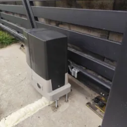 Zamontowany automat do bramy przesuwnej, widoczne mocowania i pianka montażowa. Brama w kolorze grafitowym.