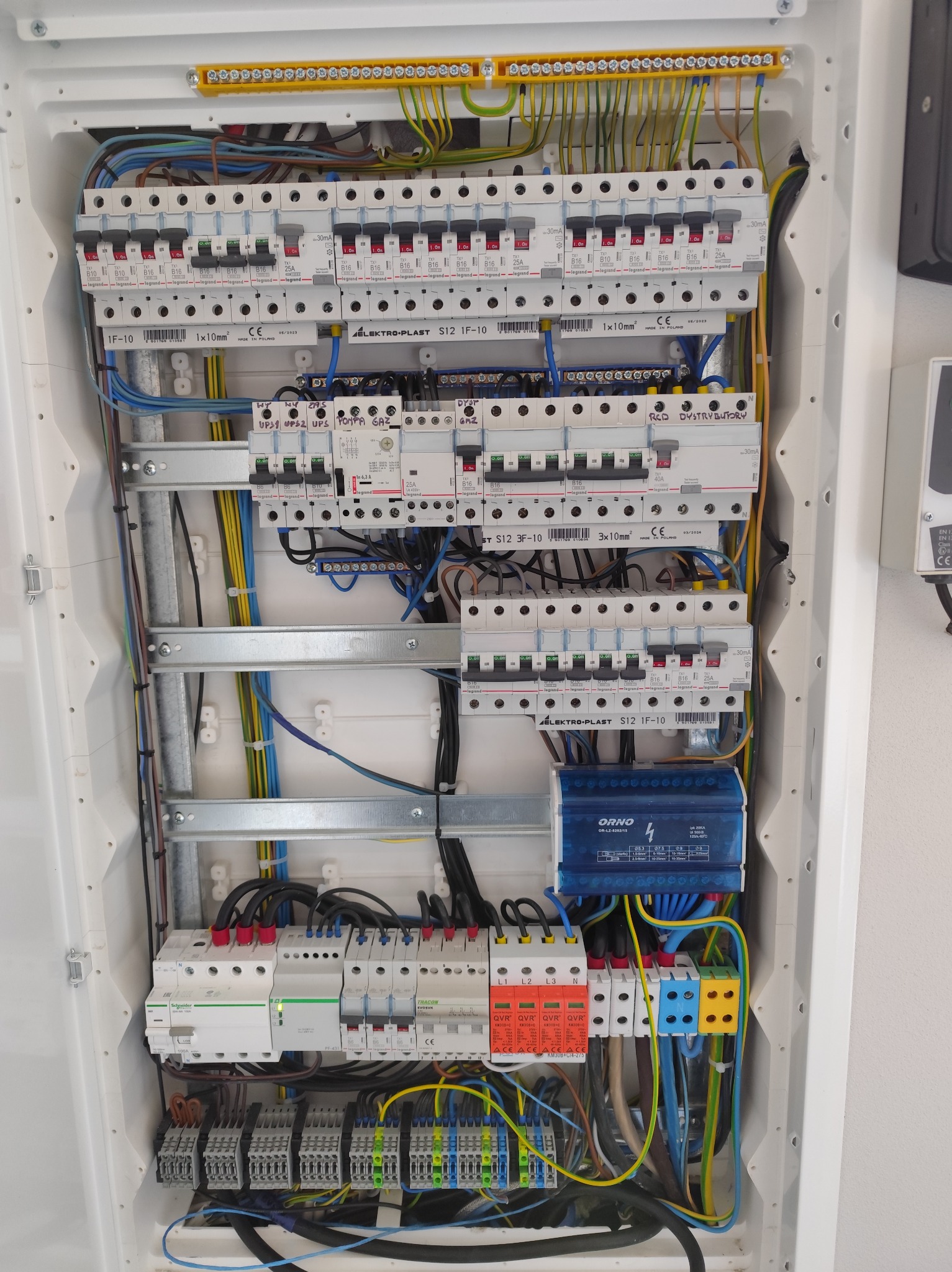 Rozdzielnica elektryczna w białej obudowie, widoczne zabezpieczenia, przewody i listwy. Instalacja wykonana schludnie, z dbałością o porządek wewnątrz szafki.