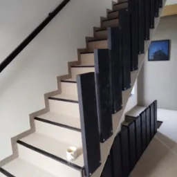 Nowoczesne schody wewnętrzne z jasną wykładziną i czarnymi elementami wykończeniowymi, na jednym ze stopni stoi biały kubek z kawą.