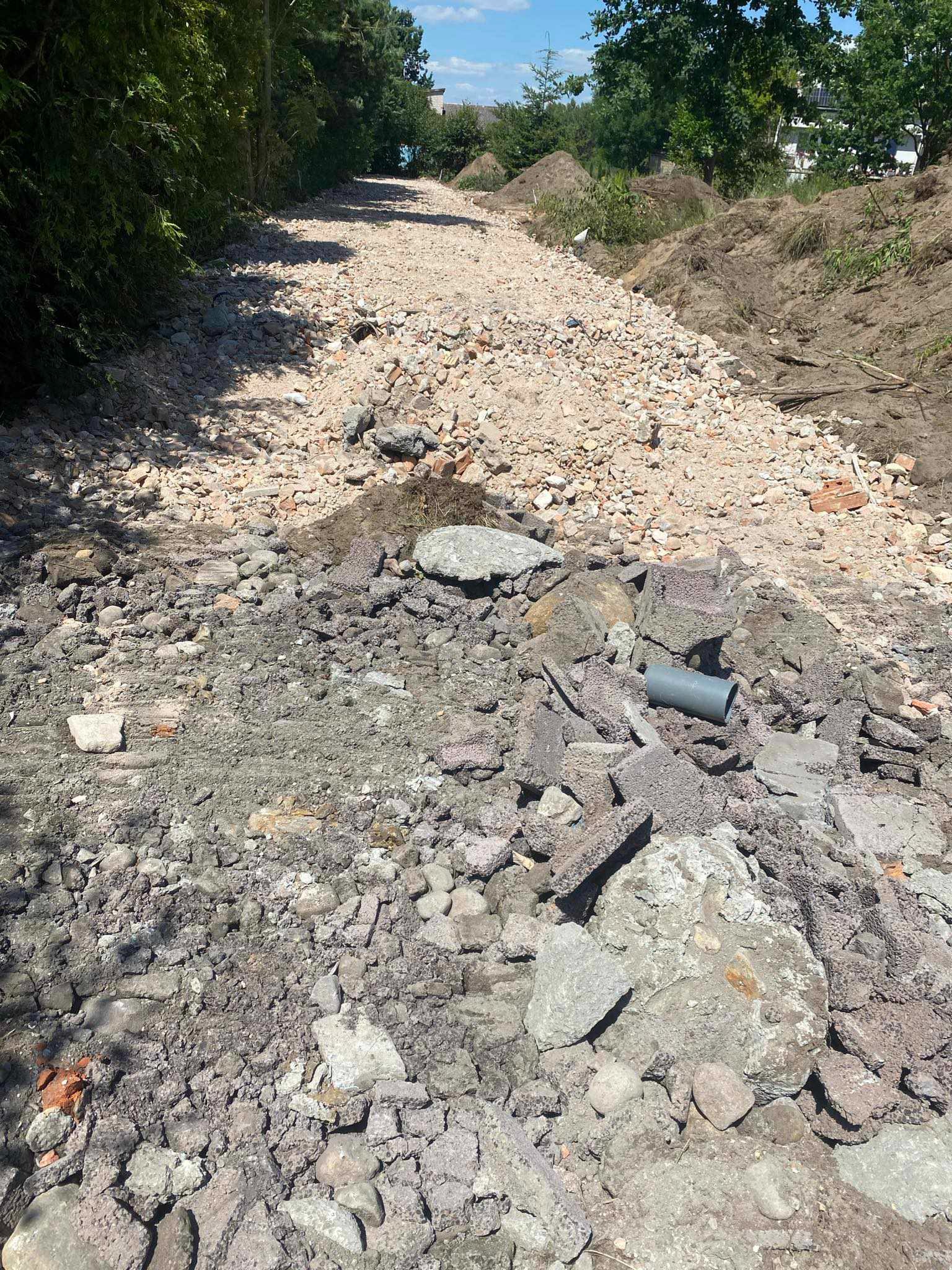 Przygotowanie terenu pod budowę: ziemia usypana w wały po bokach, na środku gruz ceglany i betonowy, widoczny fragment rury kanalizacyjnej.