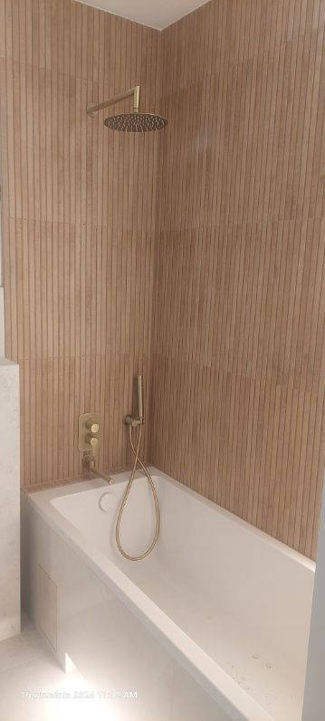 Nowoczesna łazienka z beżowymi, pionowo ułożonymi płytkami imitującymi drewno, złota bateria podtynkowa i deszczownica nad białą wanną