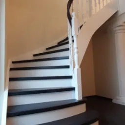 Zakręcone schody z czarnymi stopniami i białymi podstopnicami oraz balustradą z ciemnym poręczą, widok z dołu na pierwszy bieg.