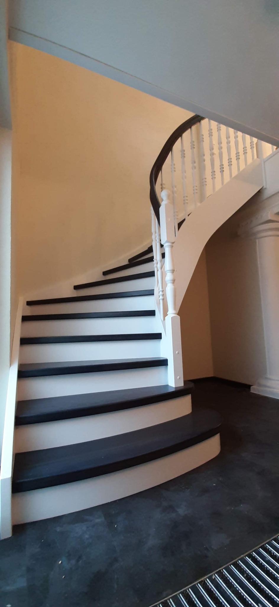 Zakręcone schody z czarnymi stopniami i białymi podstopnicami oraz balustradą z ciemnym poręczą, widok z dołu na pierwszy bieg.