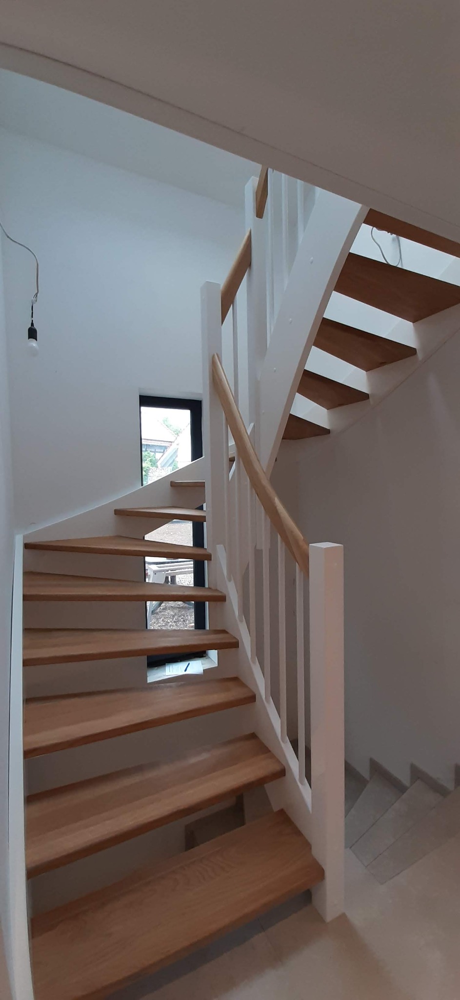 Wewnętrzne schody drewniane z białymi balustradami w domu w Gorzowie Wielkopolskim, widoczne z dołu, z oknem w tle.