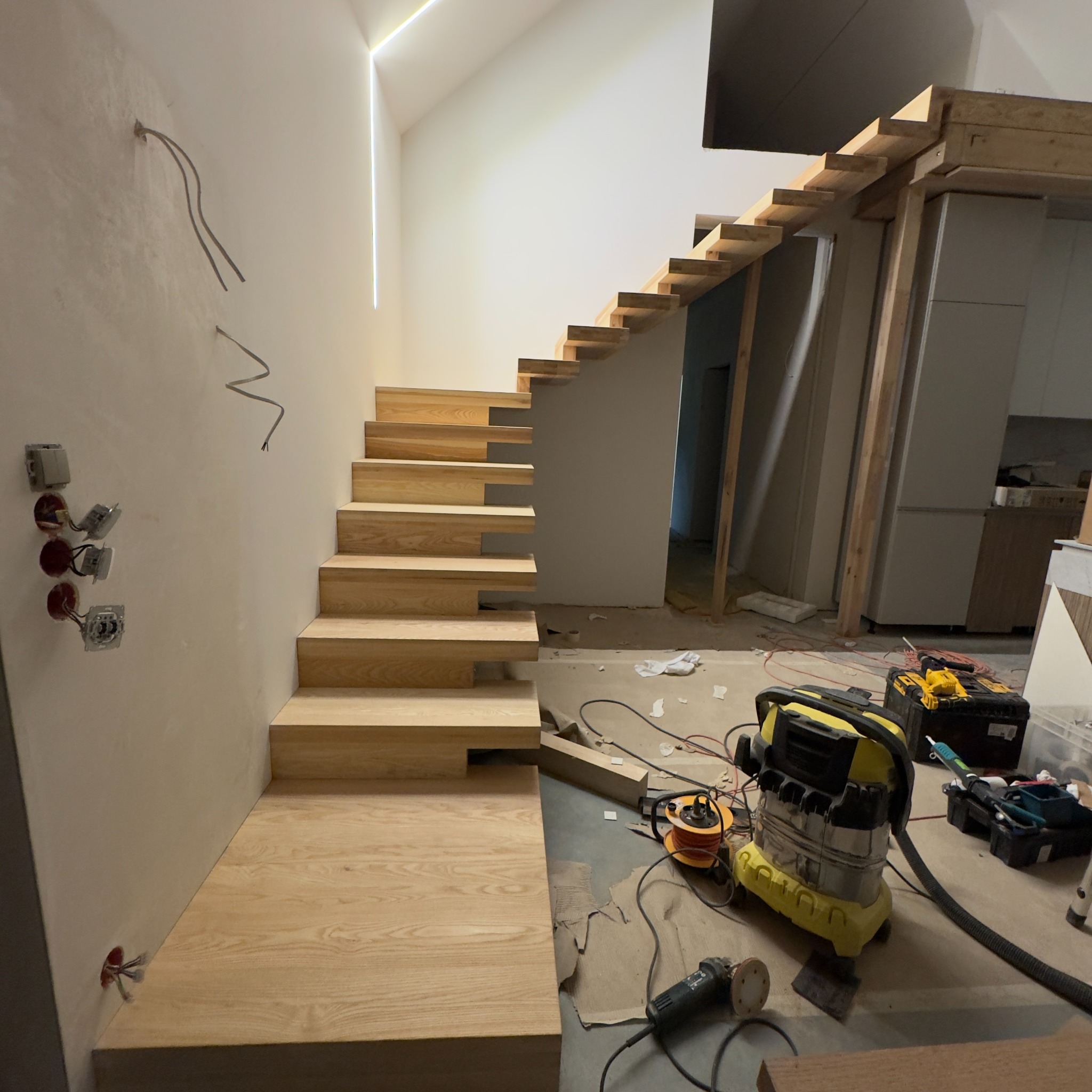 Montaż ażurowych schodów z jasnego drewna w nowoczesnym wnętrzu. Widoczne narzędzia i niedokończone wykończenia ścian.