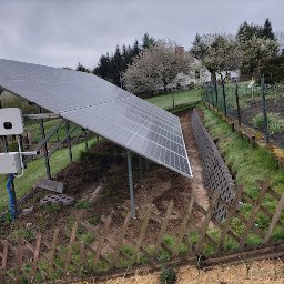 PVhurt.pl Anna Kulikowska - Panel słoneczny na stelażu z falownikiem zamontowany na zboczu ogrodu, widoczny fragment muru oporowego i drewnianego płotu.