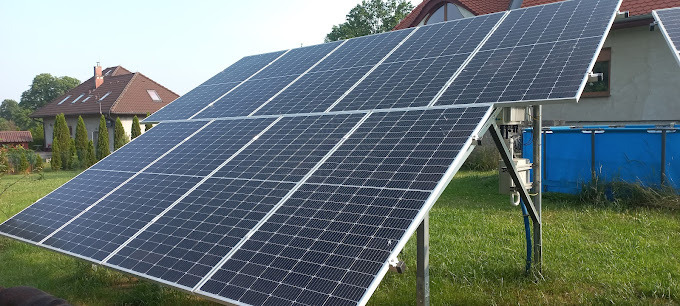 Instalacja paneli słonecznych na metalowej konstrukcji w ogrodzie, z domem jednorodzinnym i basenem w tle.