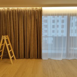 Handyman pl - Montaż zasłon: drewniana drabina oparta o ścianę z brązowymi, aksamitnymi zasłonami, obok okna z białymi, prześwitującymi firankami, widoczny parkiet na podłodze, oświetlenie LED podsufitowe.