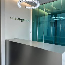Handyman pl - Nowoczesna recepcja biurowa z metalowym blatem, szklanymi ścianami działowymi i designerską lampą sufitową w kształcie pierścienia, logo firmy 'Cosmo Trade' na ścianie.