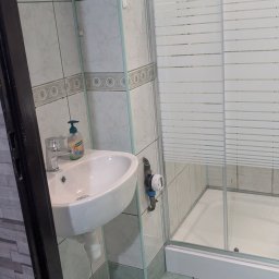 Hydraulik -opolskie - Wykończona łazienka z umywalką, kabiną prysznicową i płytkami w odcieniach zieleni. Widoczne rury doprowadzające wodę i licznik.