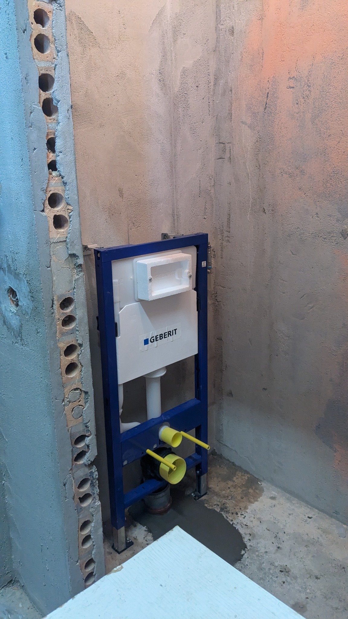 Stelaż podtynkowy Geberit zamontowany w surowym stanie, widoczne żółte rury i fragment ściany z pustaków.