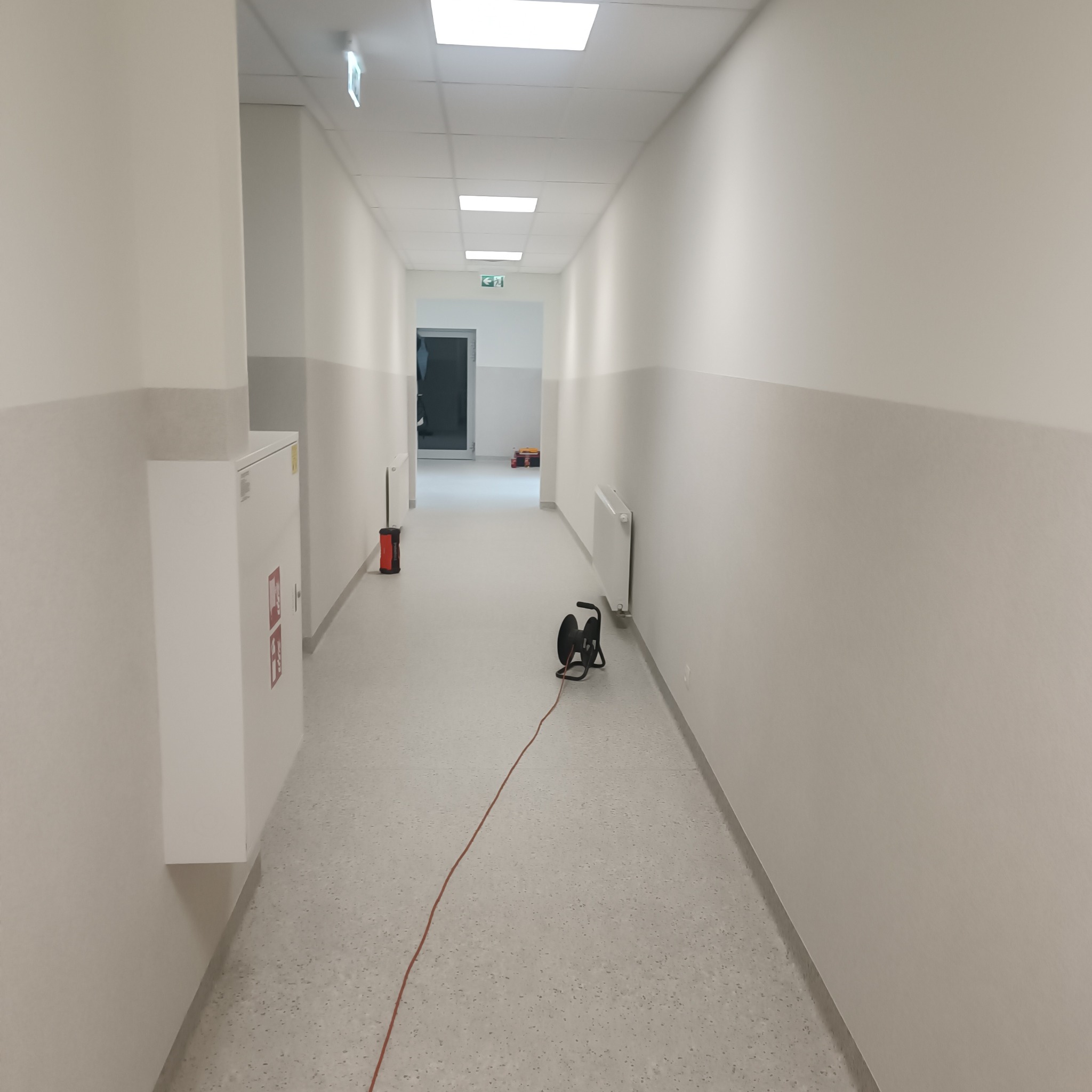 Korytarz w budynku po remoncie, z widocznym sprzętem elektrycznym, grzejnikiem i szafką hydrantową