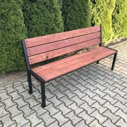 Usługi Stolarskie Konieczny - Nowoczesna ławka parkowa z jesionowymi deskami w kolorze ciemnego orzecha i czarną metalową konstrukcją, ustawiona na brukowanym chodniku przed rzędem zielonych krzewów.