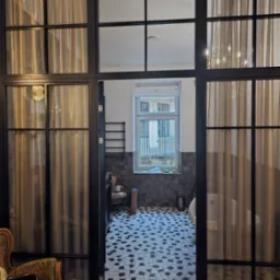 Czarne, przeszklone drzwi wewnętrzne z zasłonami, prowadzące do łazienki z mozaikową podłogą i widokiem na zewnątrz.